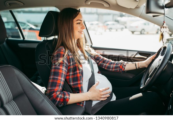 Pregnant happy woman driving with safety belt on in\
the car.