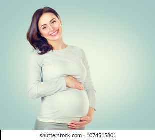 Pregnant happy Woman touching her belly. Pregnant middle aged mother portrait, caressing her belly and smiling close-up. Healthy Pregnancy concept, Gravid brunette female on blue background