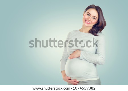 Pregnant happy Woman touching her belly. Pregnant middle aged mother portrait, caressing her belly and smiling close-up. Healthy Pregnancy concept, brunette expectant female on blue background
