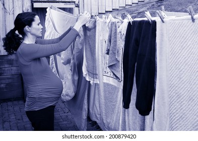 Pregnant Housewife Woman Doing Housework Pegging Out Washing To Dry On Clothes Line During Pregnancy.Concept Photo Of Pregnancy, Pregnant Woman Lifestyle And Health Care.copyspace