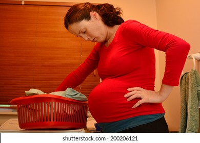 Pregnant Housewife Woman (female Age 30-40) Doing Housework, Washing Family Clothes, During Pregnancy.Concept Photo Of Pregnancy, Pregnant Woman Lifestyle And Health Care. Real People. Copy Space