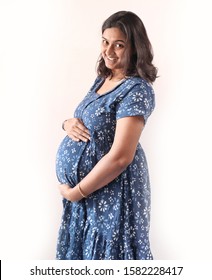 A pregnant indian lady with blue dress and hands on belly.