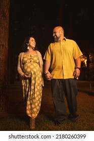 Pregnant Latin Couple Walking Hand In Hand Watching Each Other In Pine Forest At Night