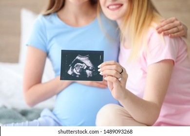 Pregnant lesbian couple with sonogram image in bedroom