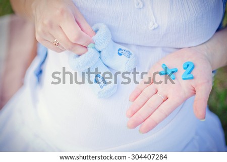 pregnant mother expecting twins keeping numbers and child socks in a hand