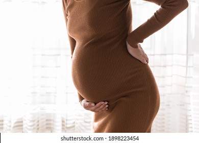 Pregnant mother get painful of back and touching her back in bedroom at home standing near window . Pregnancy healthcare concept.