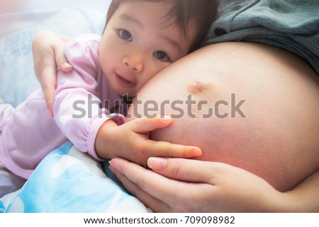 Pregnant mother and her child. A child is hugging her pregnant mother. Listening to baby's heartbeat.