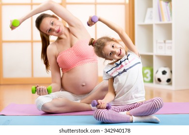 Pregnant Mother And Her Daughter Child Doing Gym Exercises With Dumbells Home