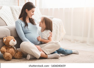 Pregnant mother and her happy daughter playing together, sitting on floor at home. Family love, motherhood and care concept, copy space - Powered by Shutterstock