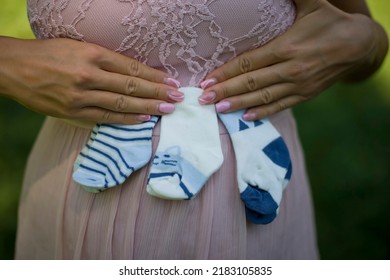 Pregnant Mother Holding A Three  Pairs Of Small Baby Socks On Stomach - Pregnancy Concept