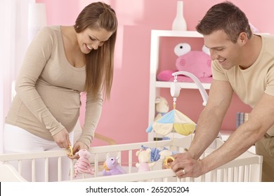 Pregnant mother and husband preparing baby's cot, smiling. - Powered by Shutterstock