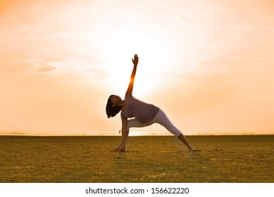 pregnant mother performing yoga on outdoor beach during sunset