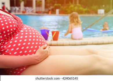 pregnant mother relax by the pool while kids play with water