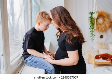 a pregnant mother and son in black clothes by the window. conversations with children about pregnancy and childbirth. the relationship between children and parents. mother's love. happy childhood. - Powered by Shutterstock