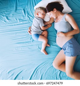 Pregnant Mother And Son Laying In Bed At Home. Pregnant For Second Time With First Child. Toddler Boy And Mom. Family In Expectation Of Baby. Pregnancy, Family, Love, Maternity Concepts.