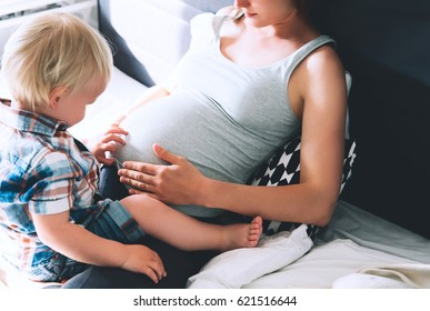 Pregnant Mother And Son Are Talking And Spending Time Together At Home. Little Child Boy Looking At Her Mother Pregnant Tummy. Pregnancy, Family, Parenthood, Preparation And Expectation Concepts.