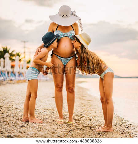Pregnant Mother with Two Kids Kissing Belly on Beach Boy Brother and Girl Sister Bikini Swimming Suits floppy Hats emotional symbol family single parent together group of people