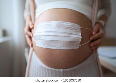 Pregnant mother use face mask covering on her abdomen for protecting fetus or baby from coronavirus, covid19, pollution, flu or pandemic. Pregnancy woman quarantine at home. 