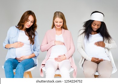 pregnant multiracial women touching bellies and looking down isolated on grey