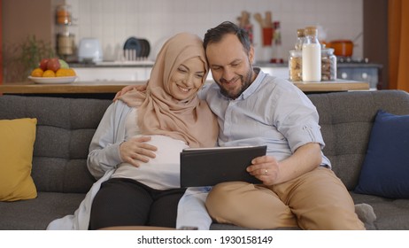 A pregnant Muslim woman wearing a headscarf and her husband use a tablet computer to exchange babies online. Online baby shopping concept. - Powered by Shutterstock