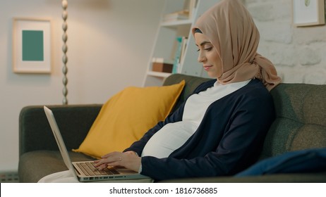 Pregnant Muslim Young Woman Doing Computer Work In Indoor Room With Lights.Concept Of Working At Home.