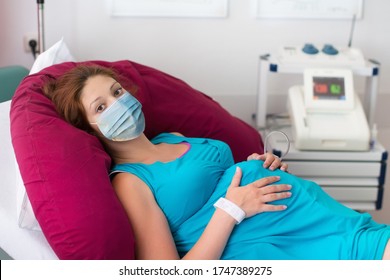 Pregnant Patient In Face Mask In A Hospital At Doctor Visit During Coronavirus Outbreak. Mother Giving Birth To Baby In Covid-19 Lockdown. Pregnancy Examination. Expecting Woman In Labor And Delivery.