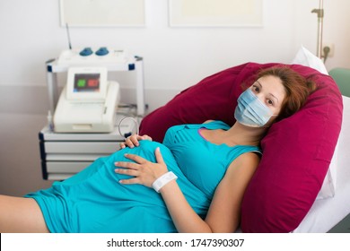 Pregnant Patient In Face Mask In A Hospital At Doctor Visit During Coronavirus Outbreak. Mother Giving Birth To Baby In Covid-19 Lockdown. Pregnancy Examination. Expecting Woman In Labor And Delivery.