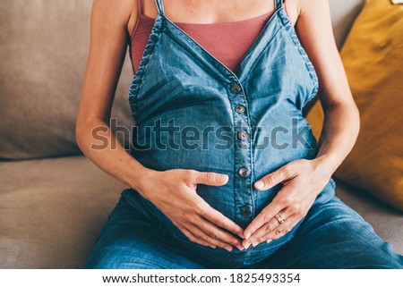 Pregnant pretty woman in a blue denim dungarees touching belly. 