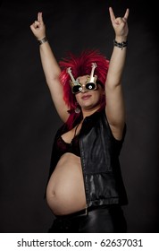 Pregnant Sexy Woman Acting As Rock Star With Red Rumpled Wig, Leather Clothes And Electrical Guitar. Concept Image For Fun And Extreme During Pregnancy. Studio Shot. See More In My Portfolio