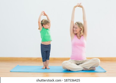 Pregnant smiling mother and daughter doing yoga together in a fitness studio - Powered by Shutterstock