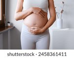 Pregnant Unrecognized Woman Dressed In A Sporty Outfit Holding Her Belly . Expecting Child. Home Indoor Interior. Concept Of Pregnancy and New Life.