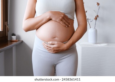 Pregnant Unrecognized Woman Dressed In A Sporty Outfit Holding Her Belly . Expecting Child. Home Indoor Interior. Concept Of Pregnancy and New Life. - Powered by Shutterstock