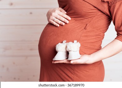 Pregnant Woman Baby Boots Closeup. Wearing Brown Stylish Dress. Maternity. Motherhood.