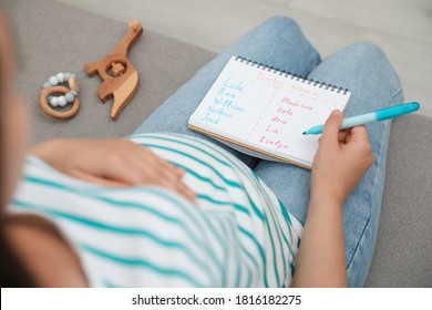 Pregnant Woman With Baby Names List Sitting On Sofa, Closeup