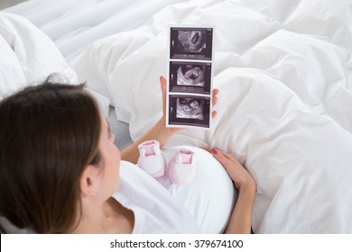 Pregnant Woman With Baby Shoes Looking At X-ray In Bedroom