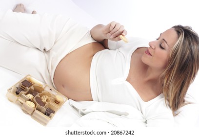 Pregnant woman in bed eating chocolate smiling - Powered by Shutterstock