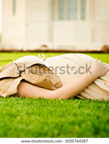 pregnant woman belly in beige dress laying on the grass