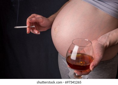 A pregnant woman with a big belly holding a glass of whiskey and a cigarette in hands on dark background. The concept of Smoking and bad habits during pregnancy