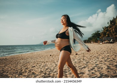 Pregnant woman in bikini on the beach happy mood. Happy pregnant woman Walking on beach. Pregnant women in prenatal beach vacations. Close up of pregnant woman belly wearing black bikini.
