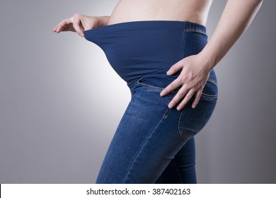Pregnant woman in blue jeans on gray background. Side view