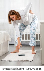 A Pregnant Woman Can Hardly Bend Down Due To Back Pain And A Large Stomach To Pick Up A Smartphone Lying On The Floor. Concept Of Everyday Difficulties Of Pregnant Women