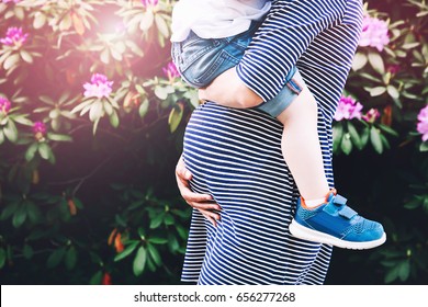 Pregnant woman with child. Mother and son on nature background, close-up. Child boy is sitting on belly of his mother, who pregnant for second time. Pregnancy, new life, family, parenthood concept.