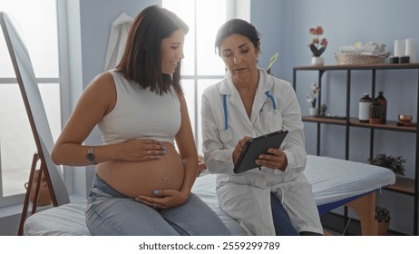 Pregnant woman consulting with female doctor using a tablet in a medical clinic room. - Powered by Shutterstock