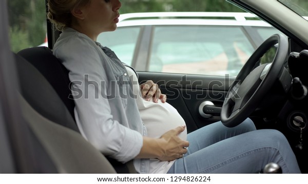 Pregnant woman deeply breathing, sitting in car,\
feeling better after belly\
pain