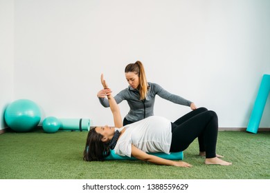 Pregnant woman doing fitness ball and pilates exercise with coach. Happy future mother preparing for childbirth.