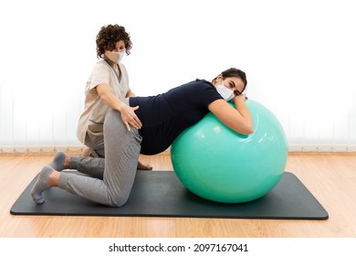 A pregnant woman doing pilates exercises with a ball with the help of her physiotherapist