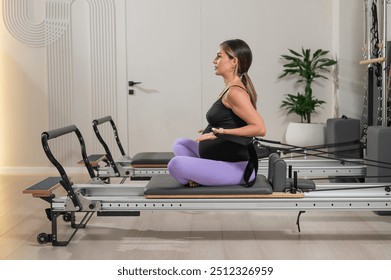 Pregnant woman doing Pilates exercises on a reformer machine.  - Powered by Shutterstock