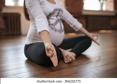 Pregnant woman doing yoga sitting on the floor in the room