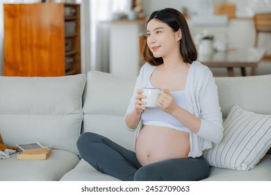 Pregnant woman drinking water or coffee sitting on sofa. Young expectant lady have rest at home with glass, copy space. Pregnancy, healthcare, thirst concept. - Powered by Shutterstock