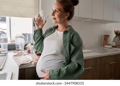 Pregnant woman drinking water while standing in the kitchen - Powered by Shutterstock